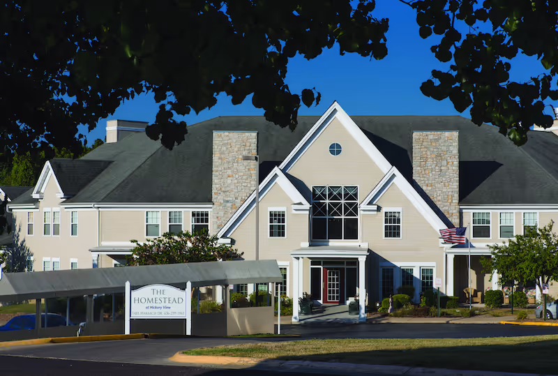 Front exterior view of Homestead At Hickory View senior living facility with entrance and sign.
