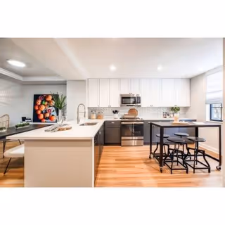 Modern open-concept kitchen with white cabinets, a center island with sink, stainless steel appliances, and a small dining table with stools.