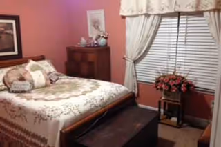 Pink themed bedroom with bed, dresser, window curtains, and a floral plant.