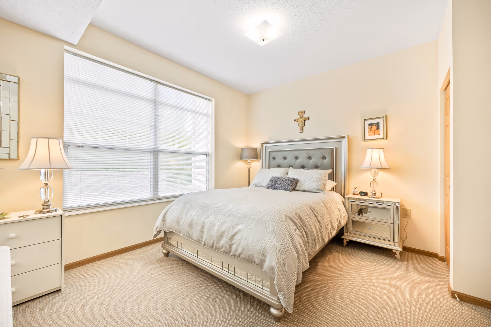 Bright, neatly staged bedroom with a tufted bed, two nightstands with lamps, and a large window with blinds.