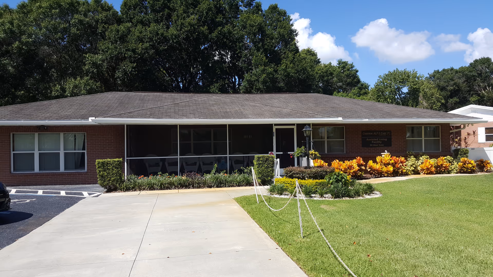 Front view of a single-story brick assisted living building with a screened porch, landscaped lawn, and driveway.