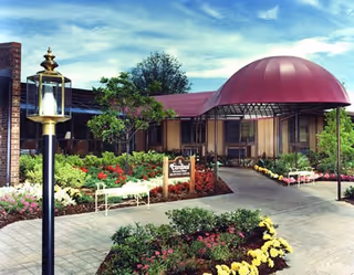 Exterior view of Cardinal Village with garden, walkway, benches, and a red-domed canopy.