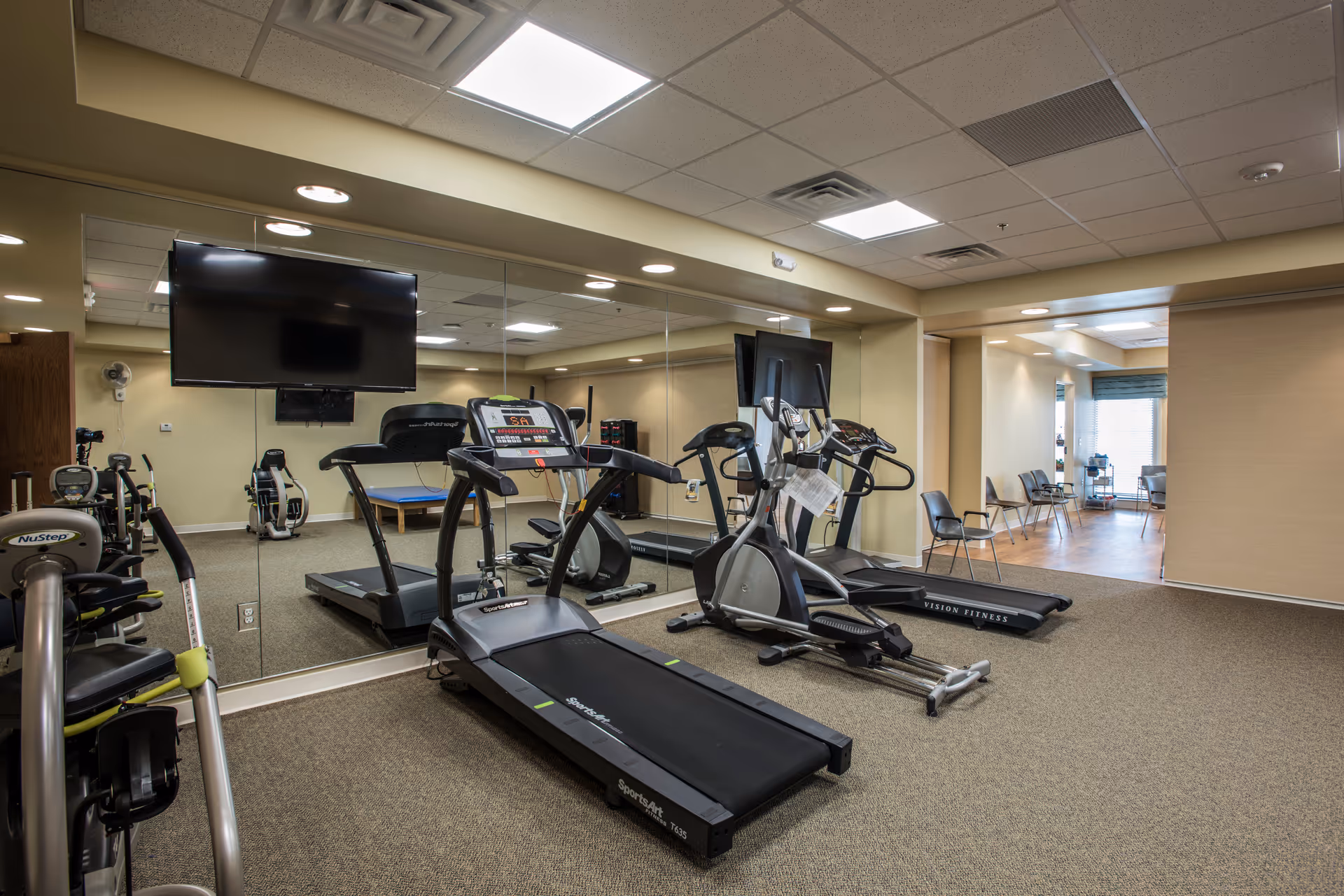 Fitness room with treadmills, elliptical machines, a mirrored wall and a wall-mounted TV.