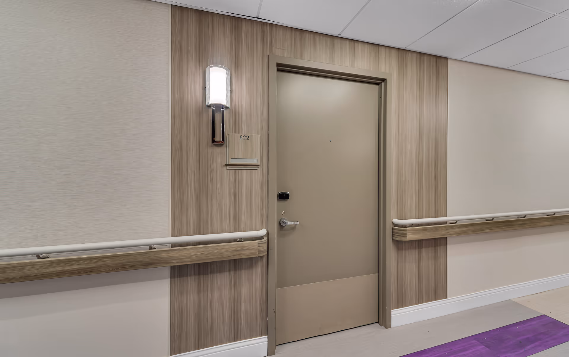 Interior corridor showing a beige apartment door labeled 822 with a wall sconce and handrails.