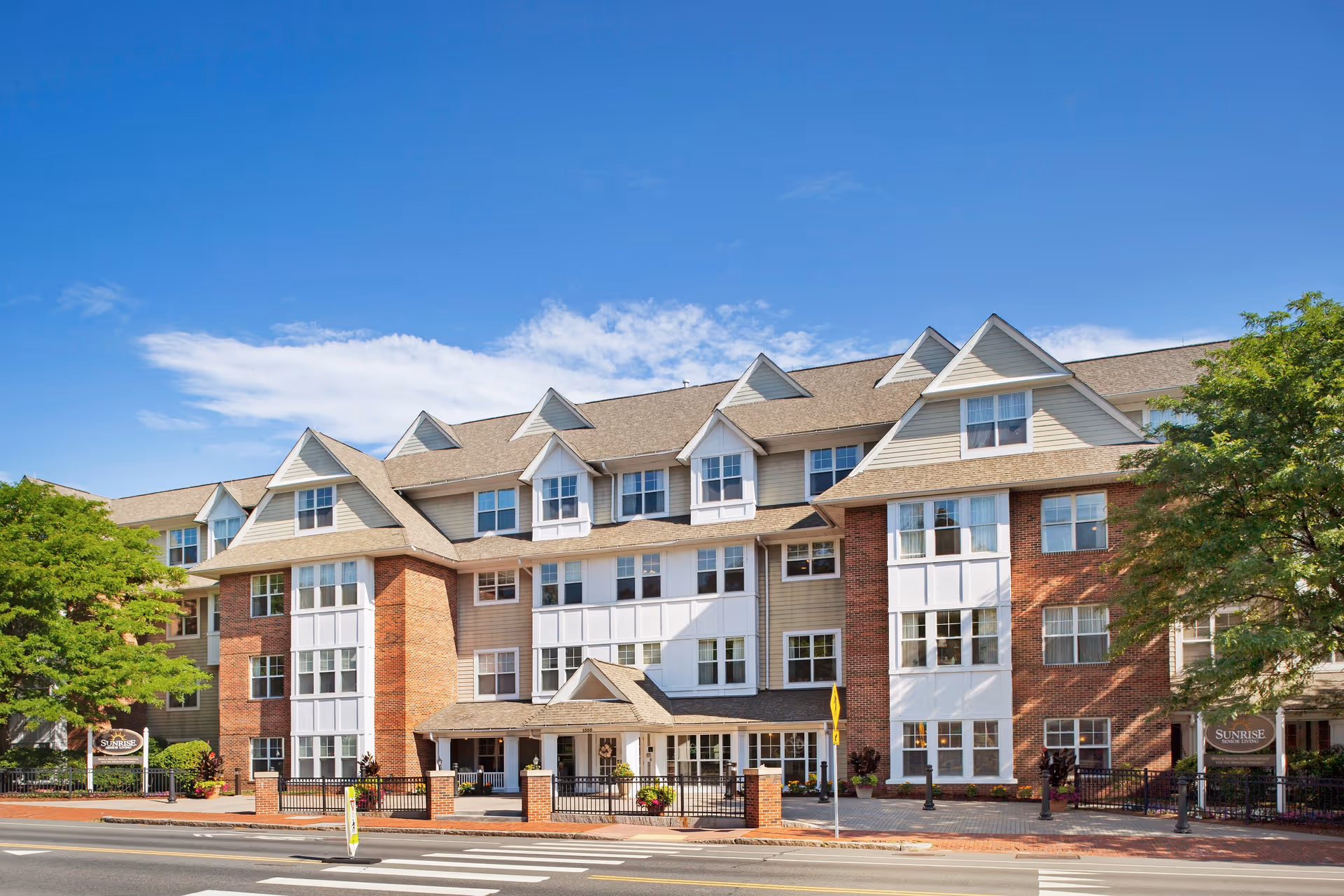 Front exterior view of Sunrise of Arlington senior living building with brick and beige siding.
