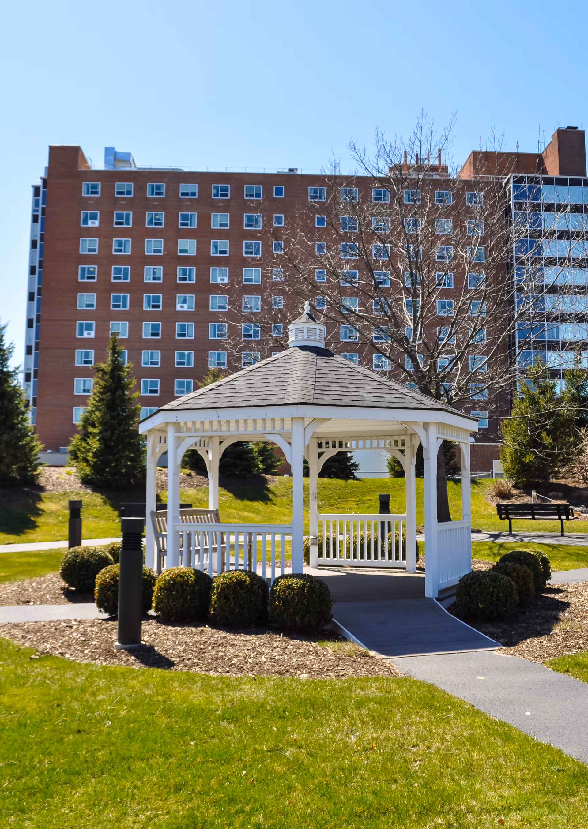 White gazebo on a grassy lawn with a multi-story brick building in the background.