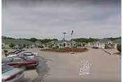 Exterior view of River Hills Village showing a circular drive, flagpole, and parked cars.