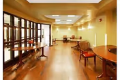 Warm, spacious dining area in a senior facility with wood floors, tables, and red chairs.