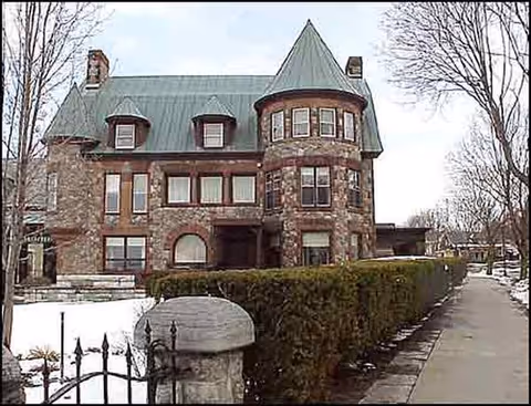 Arkell Hall exterior, a stone brick building with turret, snow on ground, and hedged fence.