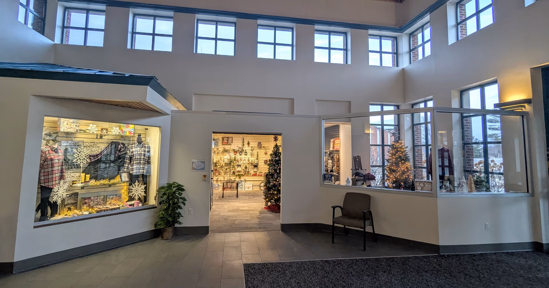 Bright two-story lobby area with storefront display windows, holiday decorations and a chair near the entrance.