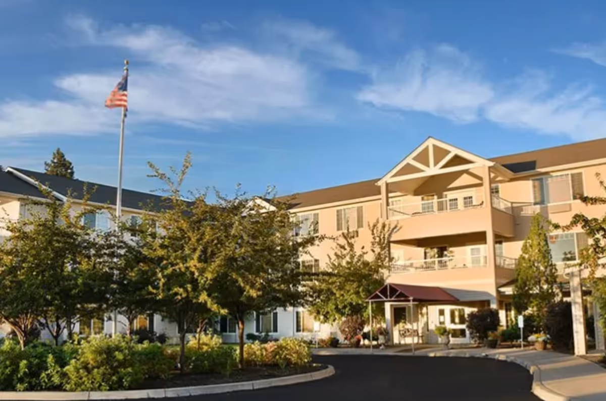 Exterior view of Fox Hollow Independent and Assisted Living building with trees and flagpole.