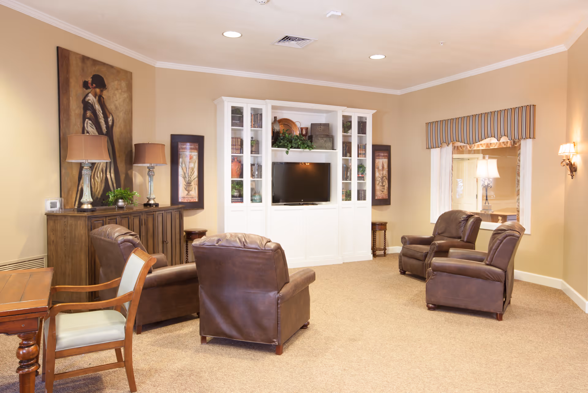 A cozy lounge with leather armchairs arranged facing a white entertainment cabinet with a TV and decorative artwork.
