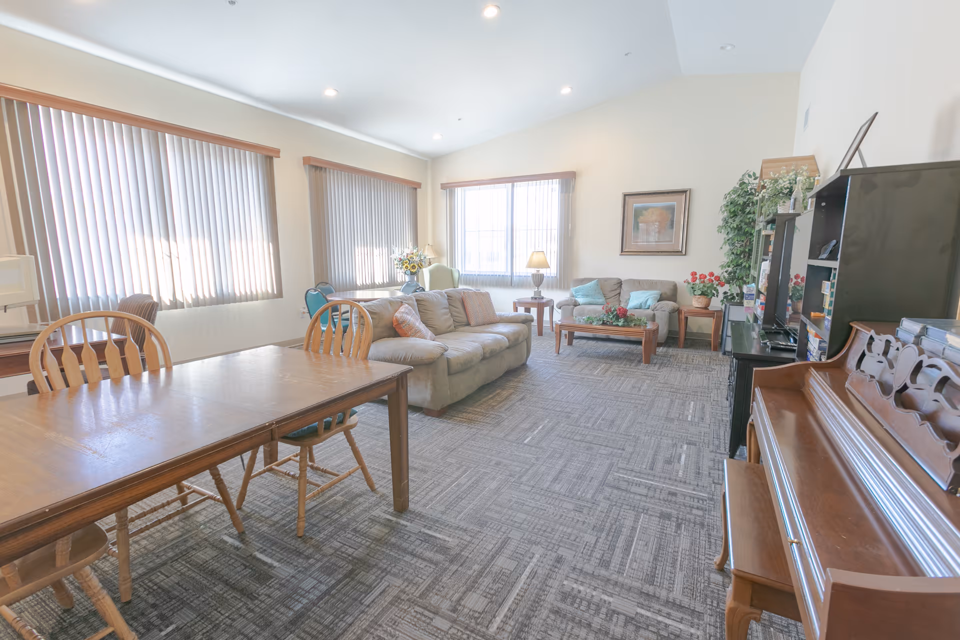 Bright communal living area with sofas, a coffee table, dining table and a piano.