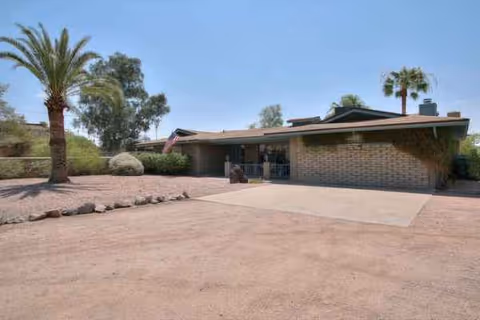 Single-story brick senior living facility entrance with desert landscaping and a wide driveway.