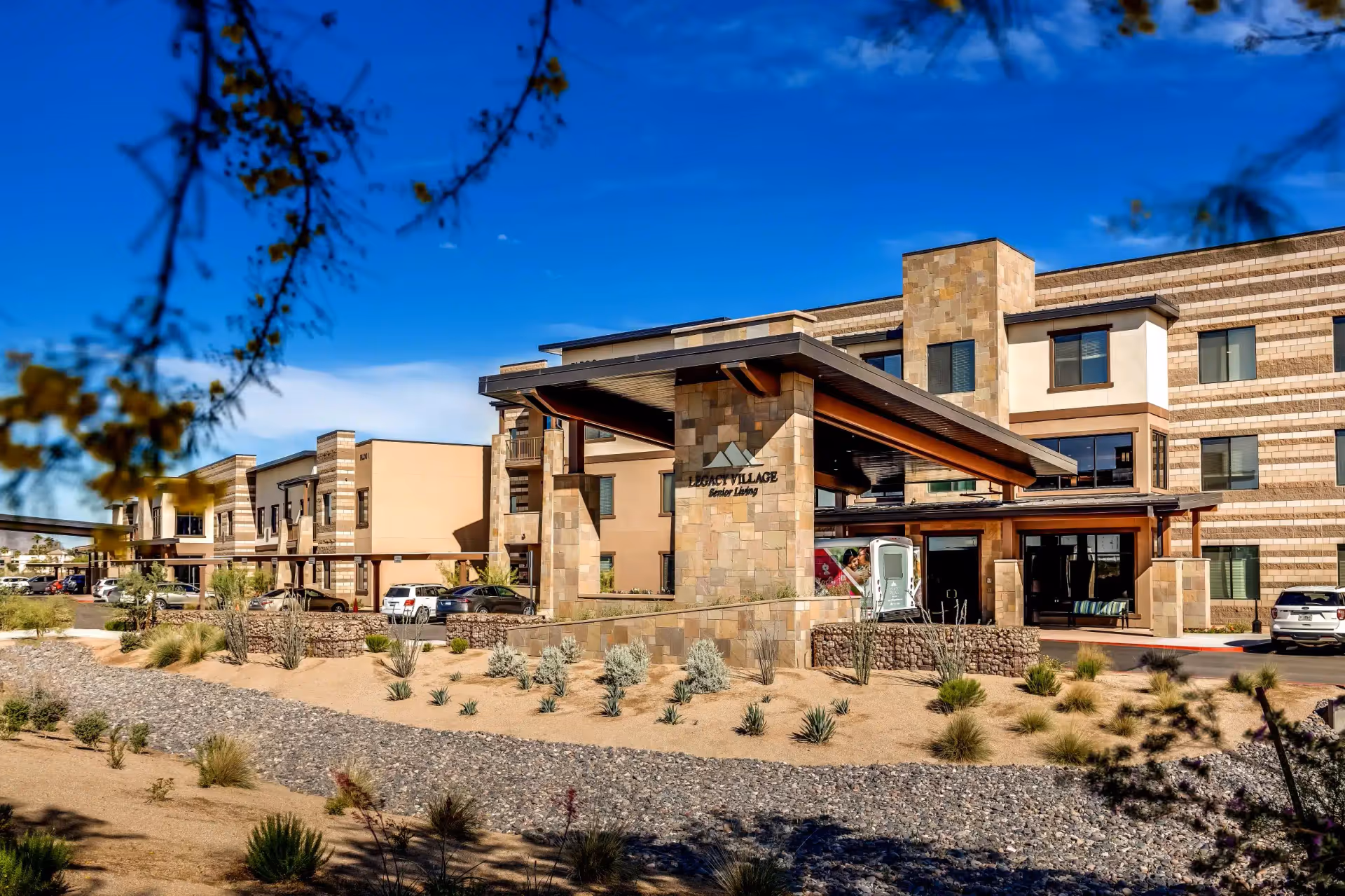 Front exterior of a three-story senior living building with a covered entrance and desert landscaping.