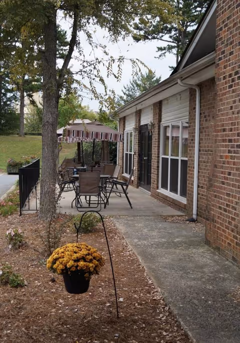 Outdoor patio area with chairs, umbrellas, and a hanging flower pot beside a brick building.