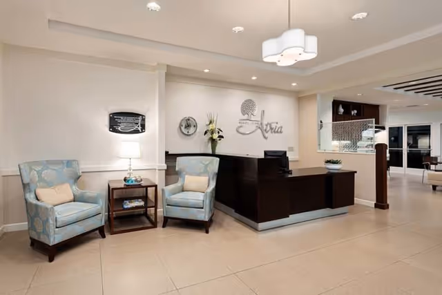 Reception lobby of Atria Palm Desert with a dark wood front desk, two patterned armchairs and wall signage.