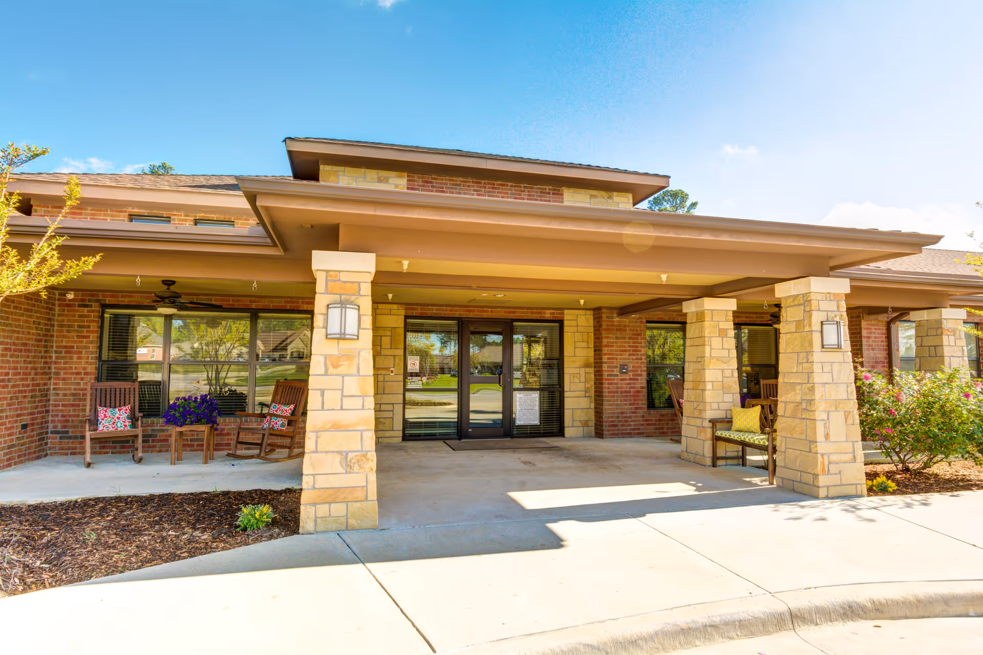 Covered entrance of Oak Hills Terrace Memory Care with stone pillars, porch seating, and glass double doors.