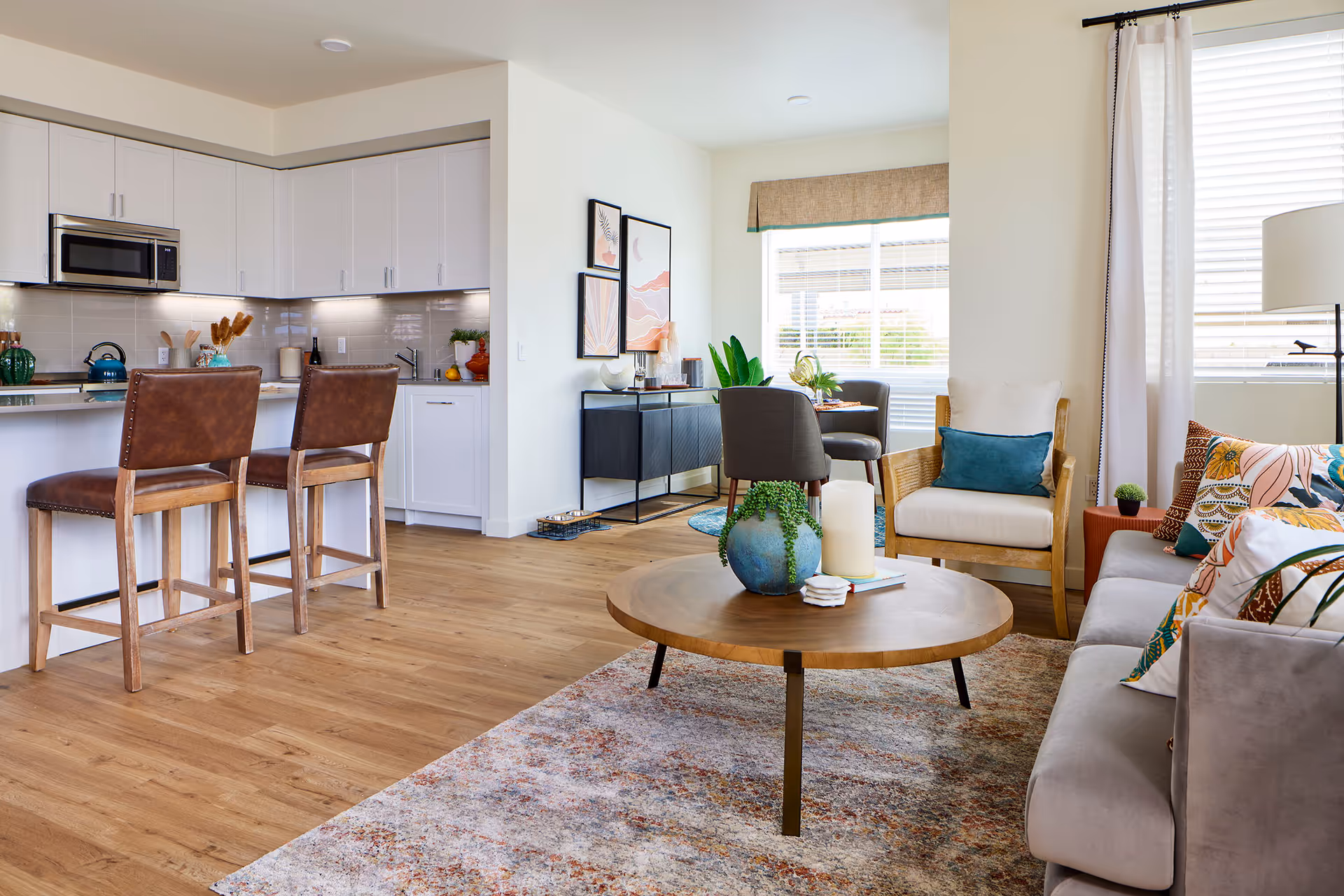 Open-plan living room and kitchen with a round wooden coffee table, sofa and armchairs, and two leather bar stools at a white kitchen island.