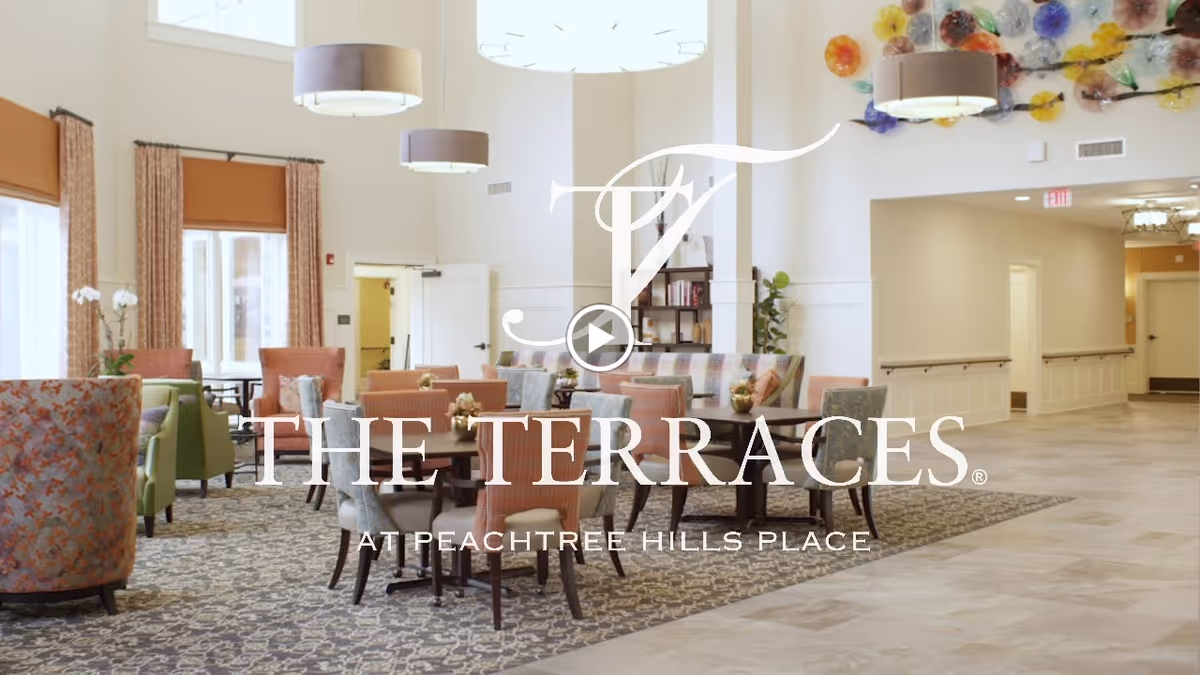 Bright communal dining/lounge with round tables, upholstered chairs, pendant lights and decorative wall art, overlaid with 'The Terraces at Peachtree Hills Place' logo.