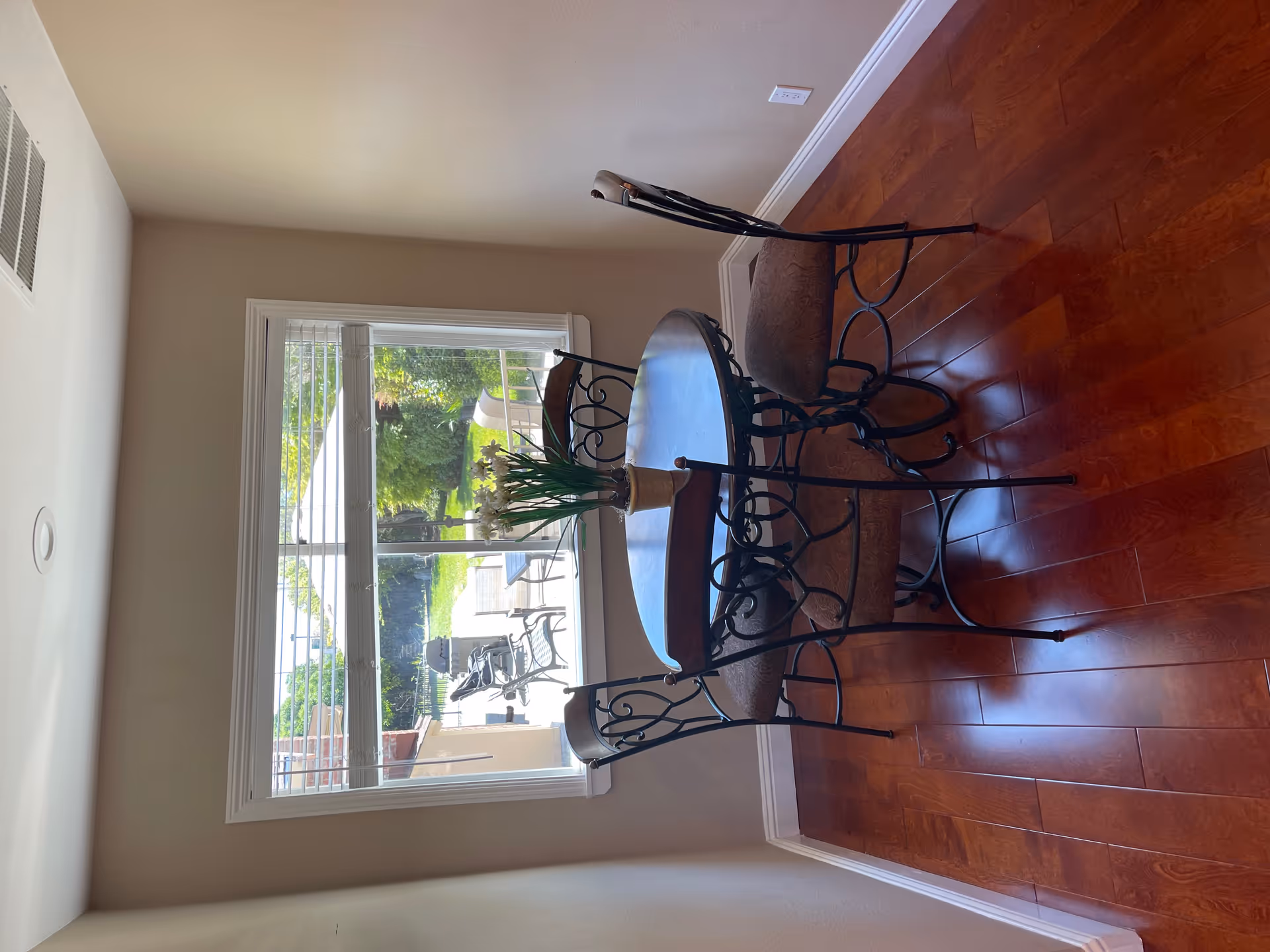 Round glass dining table with wrought-iron chairs in a sunlit dining area.