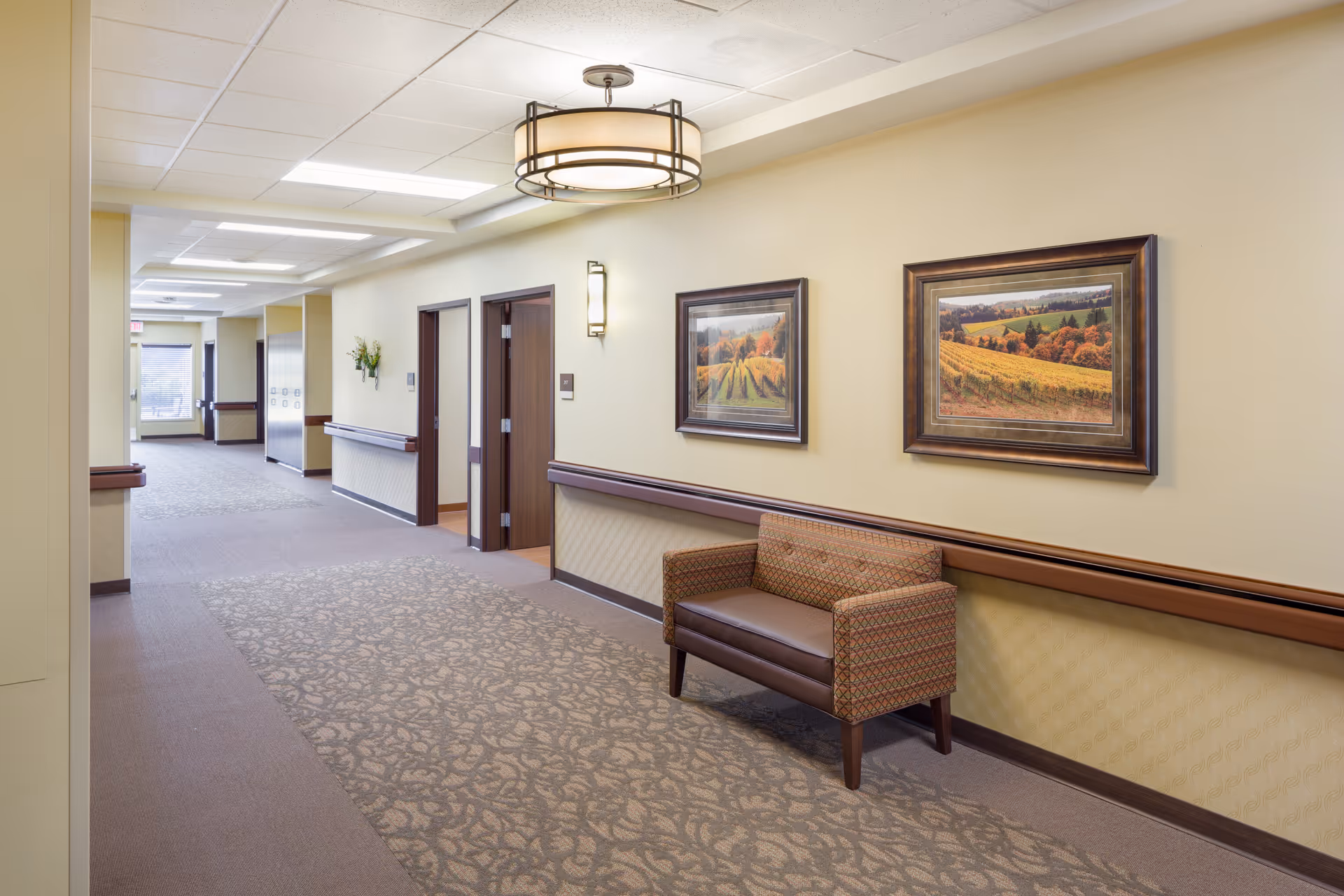 A well-lit hallway in a senior living facility with seating and framed artwork.