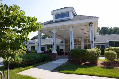 The Meadows senior living facility front entrance with white columns and landscaping.