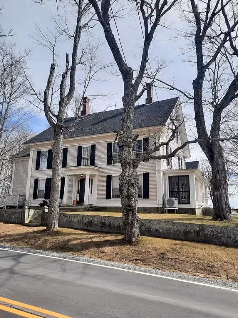 White colonial-style senior living building facing a street, with leafless trees in front.