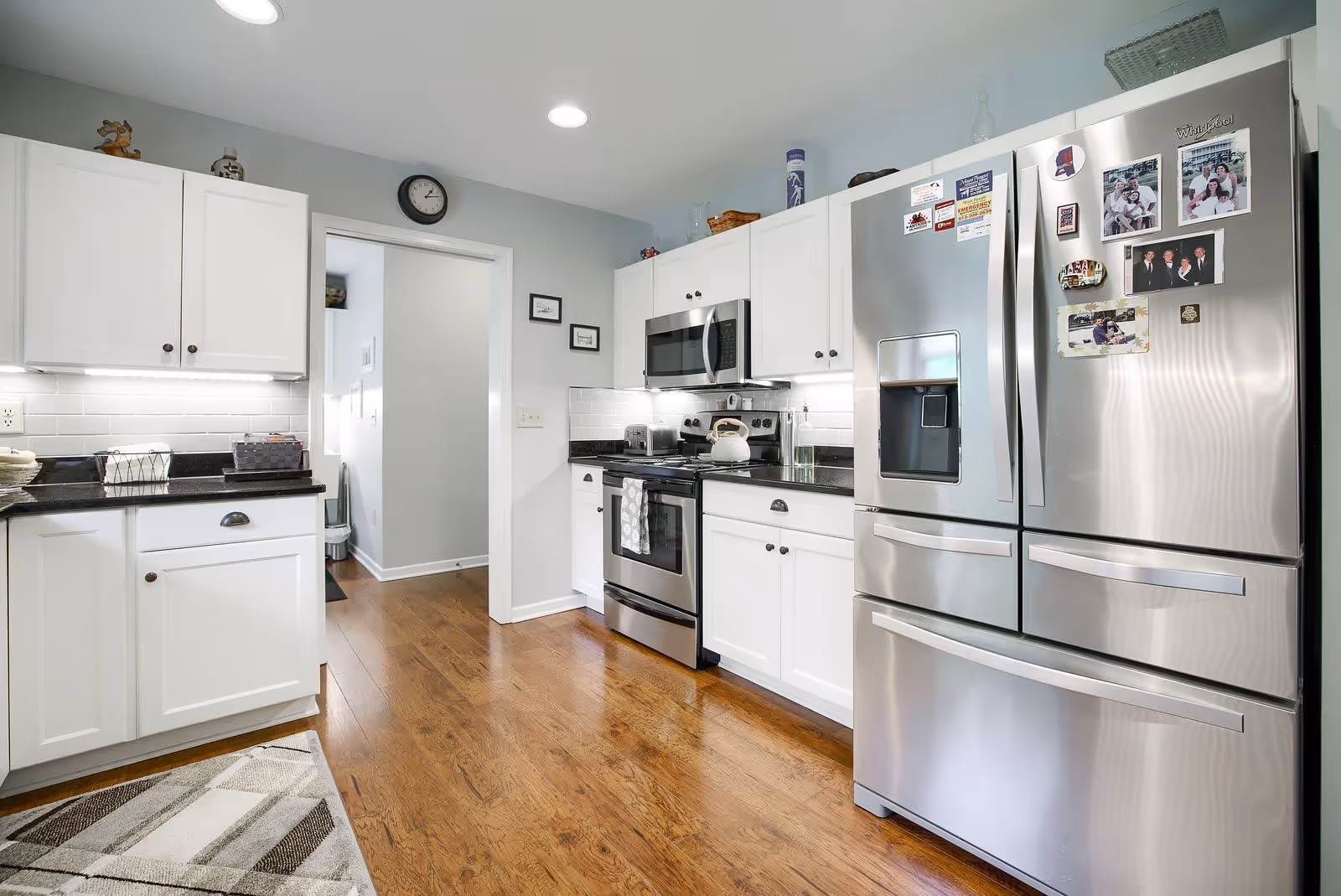 Bright modern kitchen with white cabinets, stainless steel refrigerator and oven, and hardwood floors.