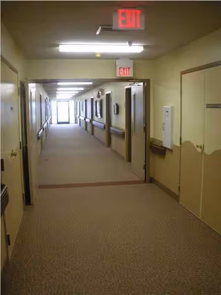 Fluorescent-lit corridor in a senior living facility with doors and exit signs.