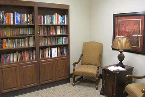 Cozy reading corner with a tall bookshelf, two chairs, a side table lamp, and framed art.