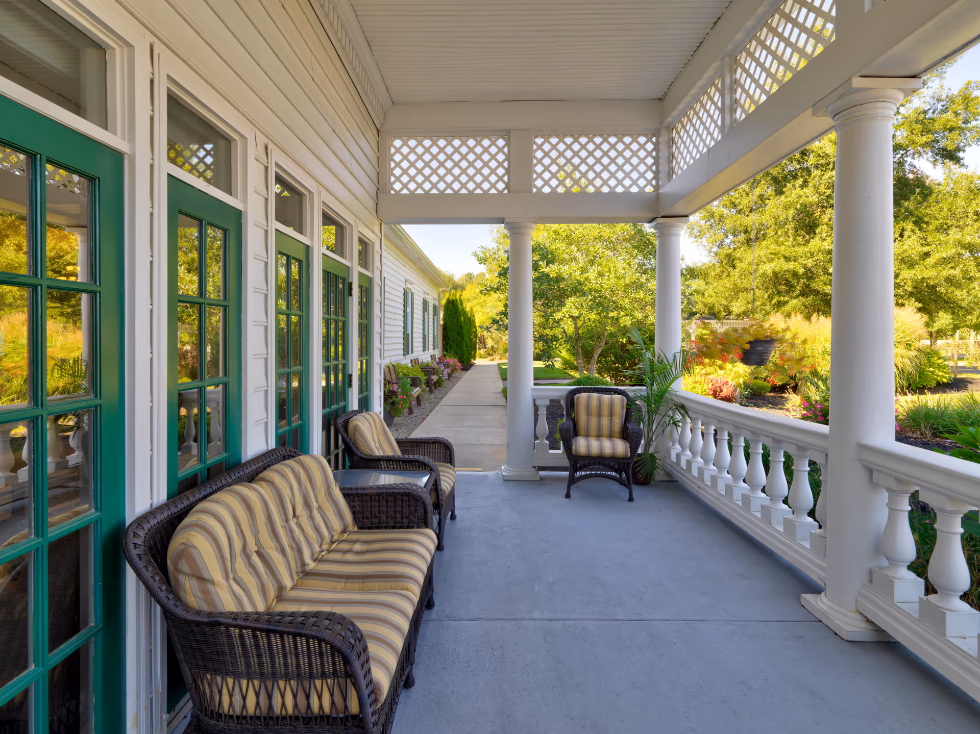 Covered porch with wicker sofa and chairs with striped cushions overlooking a landscaped garden.