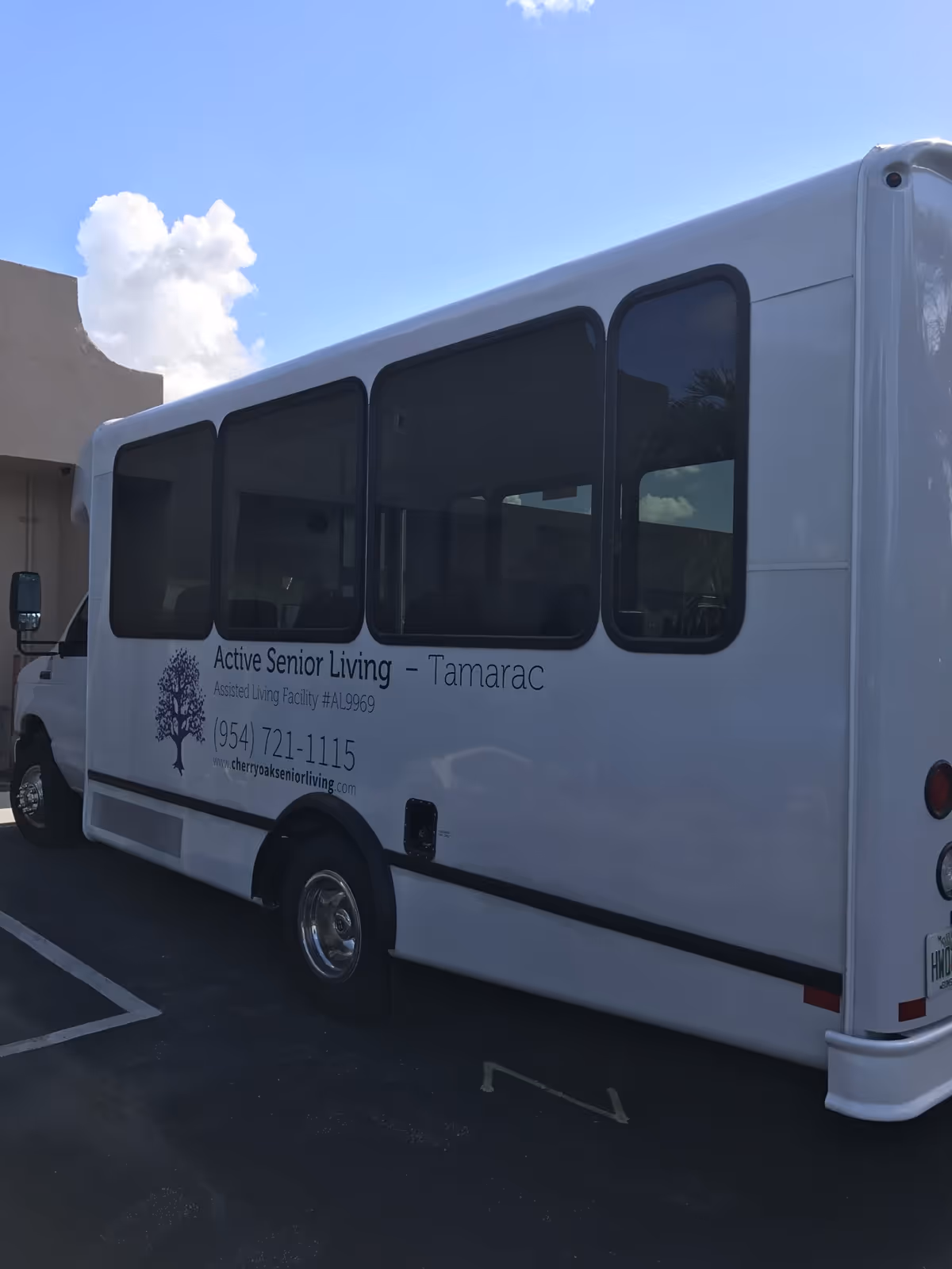 White shuttle bus parked outside with signage for Active Senior Living - Tamarac, including contact phone number and website on the side of the bus.