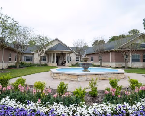 Exterior view of Gurnee Place Memory Care Community featuring a central fountain and landscaped grounds.