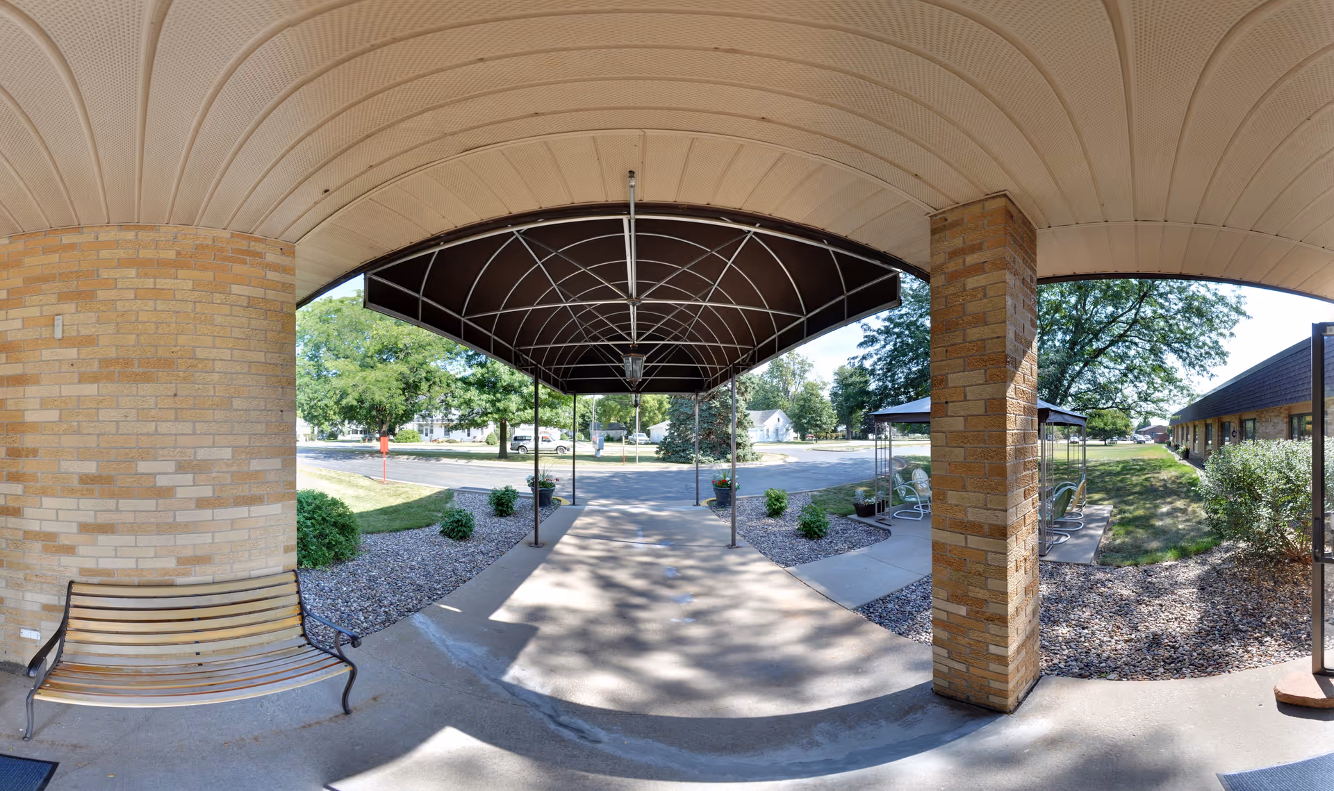 Covered entrance canopy and walkway with brick columns, a bench, and landscaping at the front of the facility.