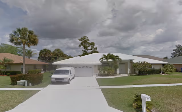 Single-story building with curved driveway, parked white van, and palm trees in the front yard.