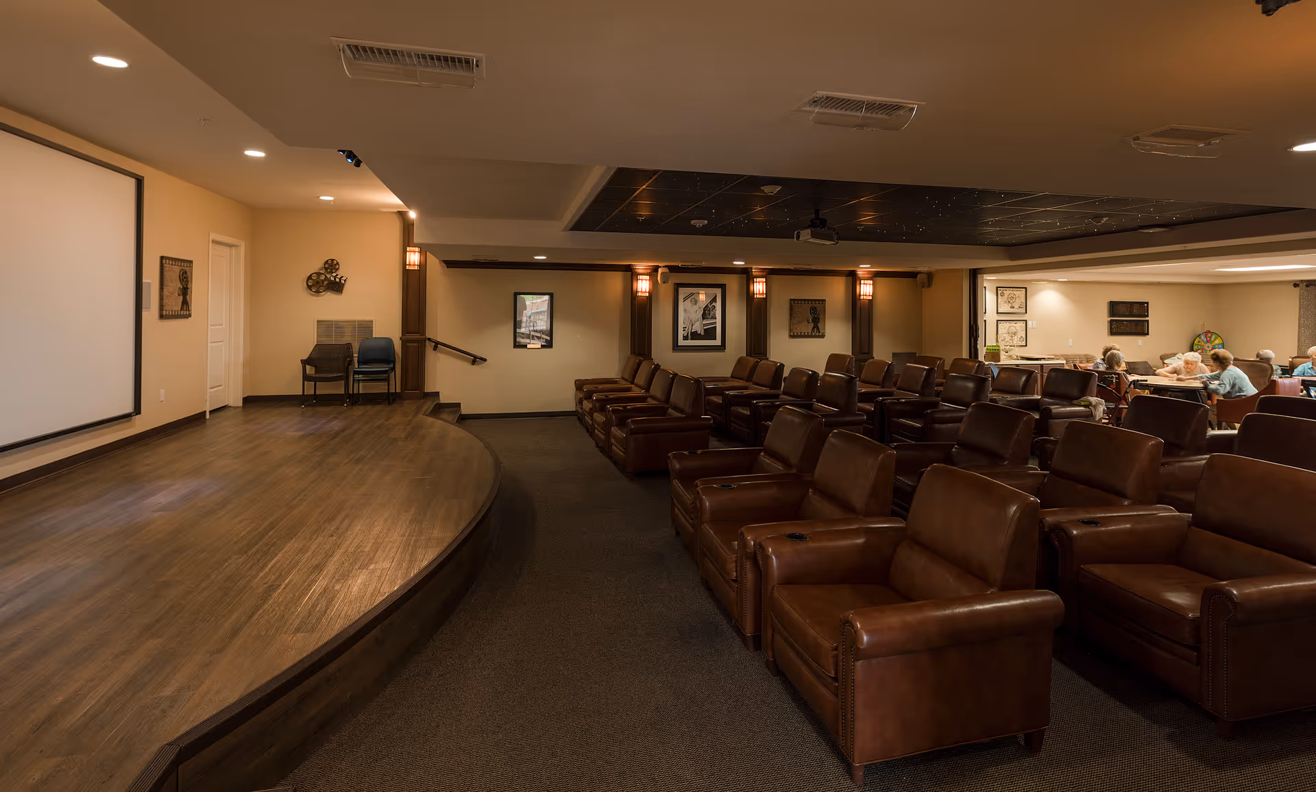 Auditorium-style screening room with a curved wooden stage, a large projection screen and rows of brown leather recliner seats.