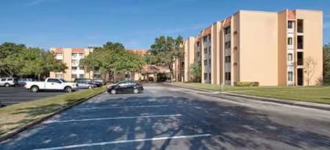 Exterior view of a multi-story senior living building with a parking lot and trees.