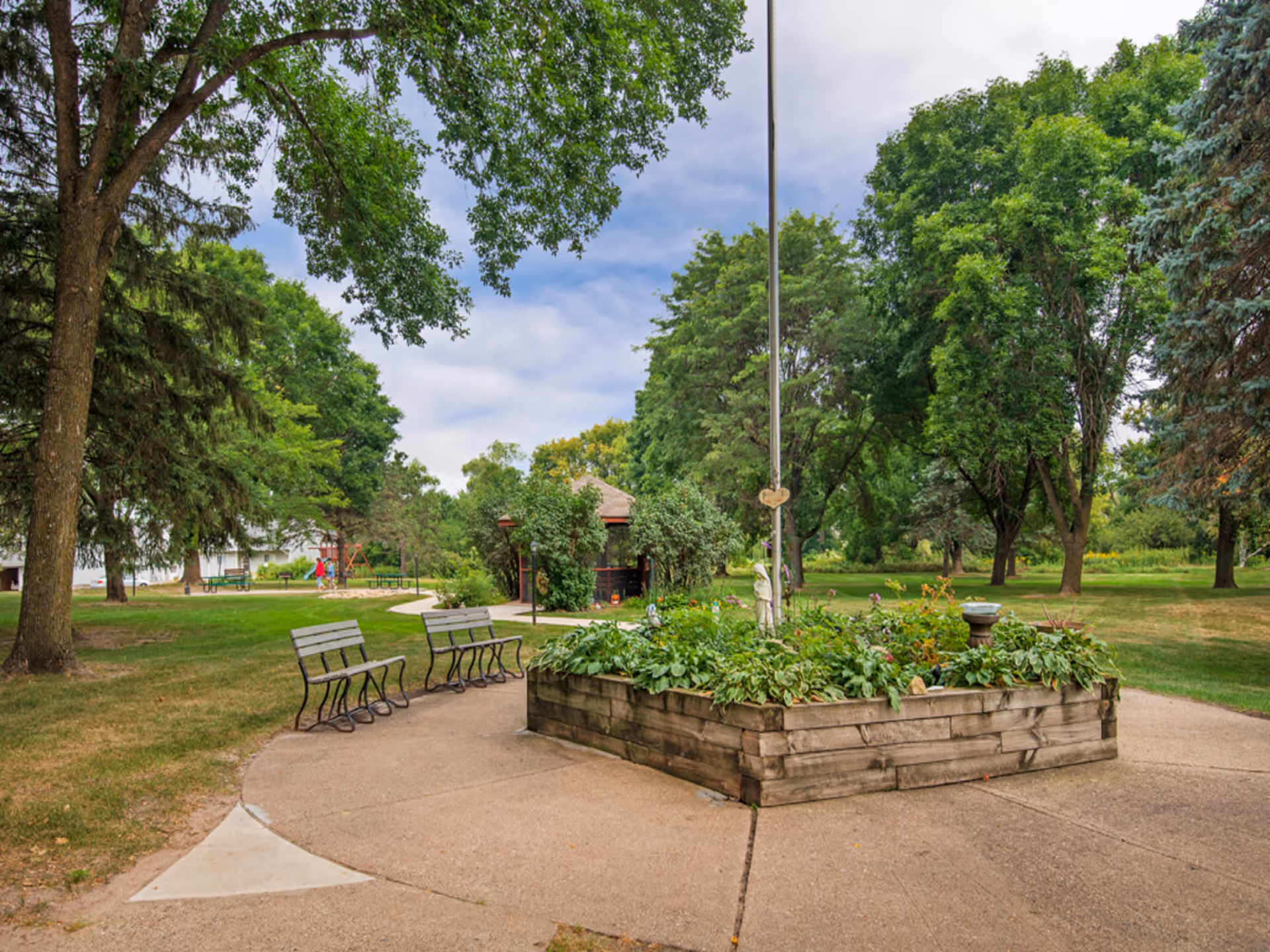 Park-like courtyard with benches, a raised wooden planter and flagpole, walking paths, and large trees.