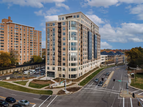 A modern tall senior living building with curved glass facade beside a busy intersection.