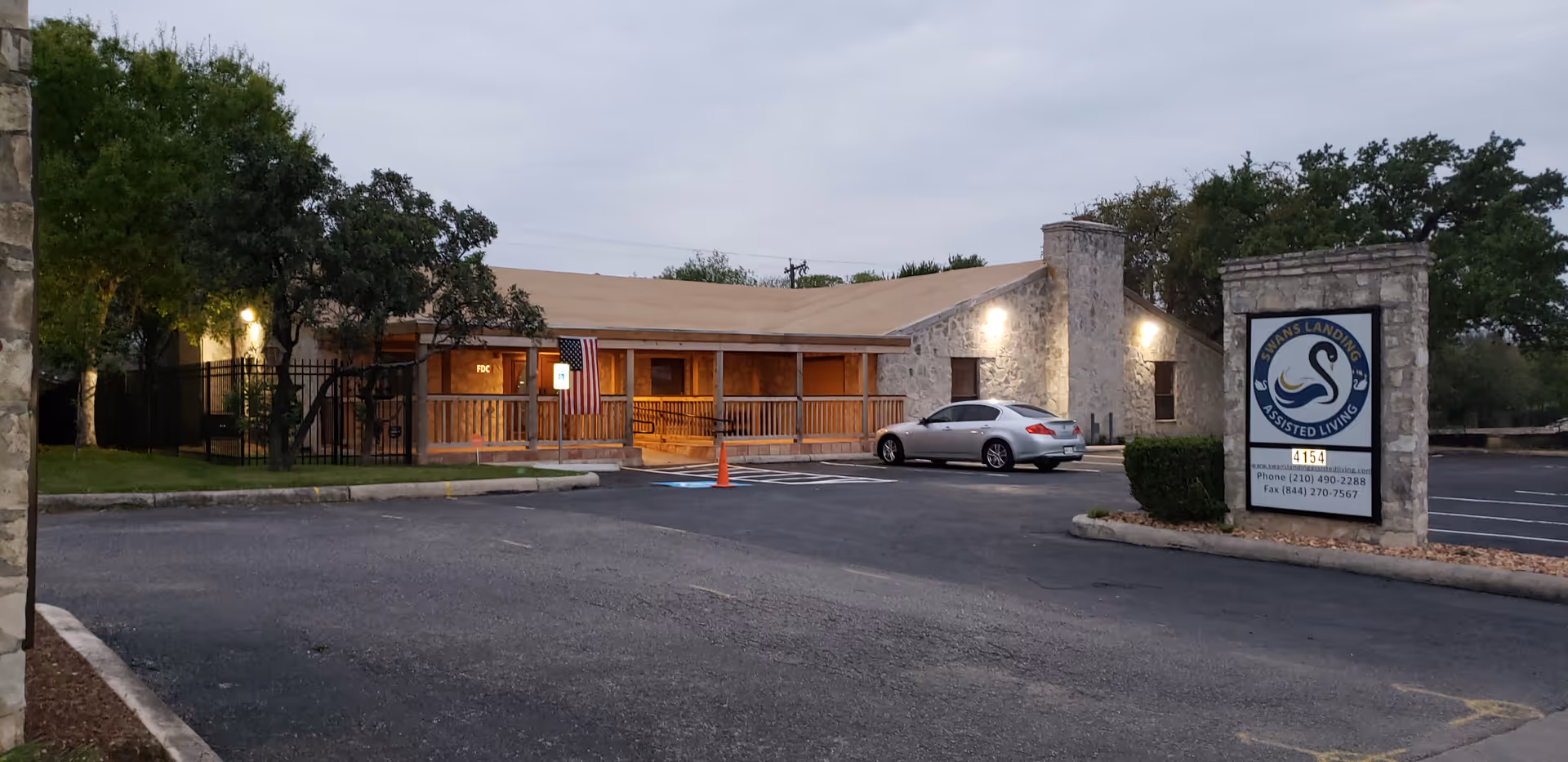 Exterior front of Swans Landing Assisted Living building with stone facade, a parking lot, parked car and the facility sign.