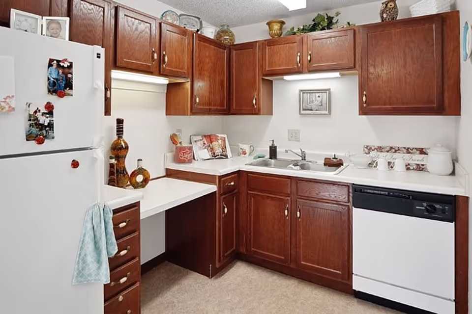 Small kitchen with white countertops, dark wood cabinets, a sink, dishwasher and refrigerator decorated with magnets and accessories.
