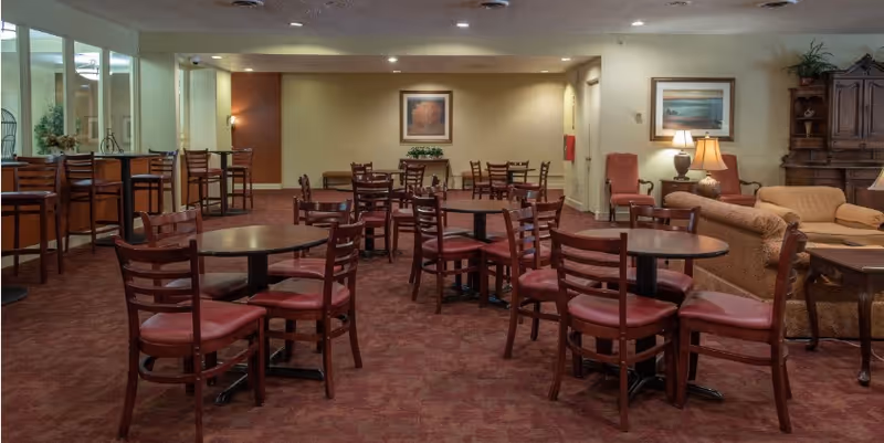 Community dining and lounge area with multiple round tables and chairs, bar seating, and sofas.