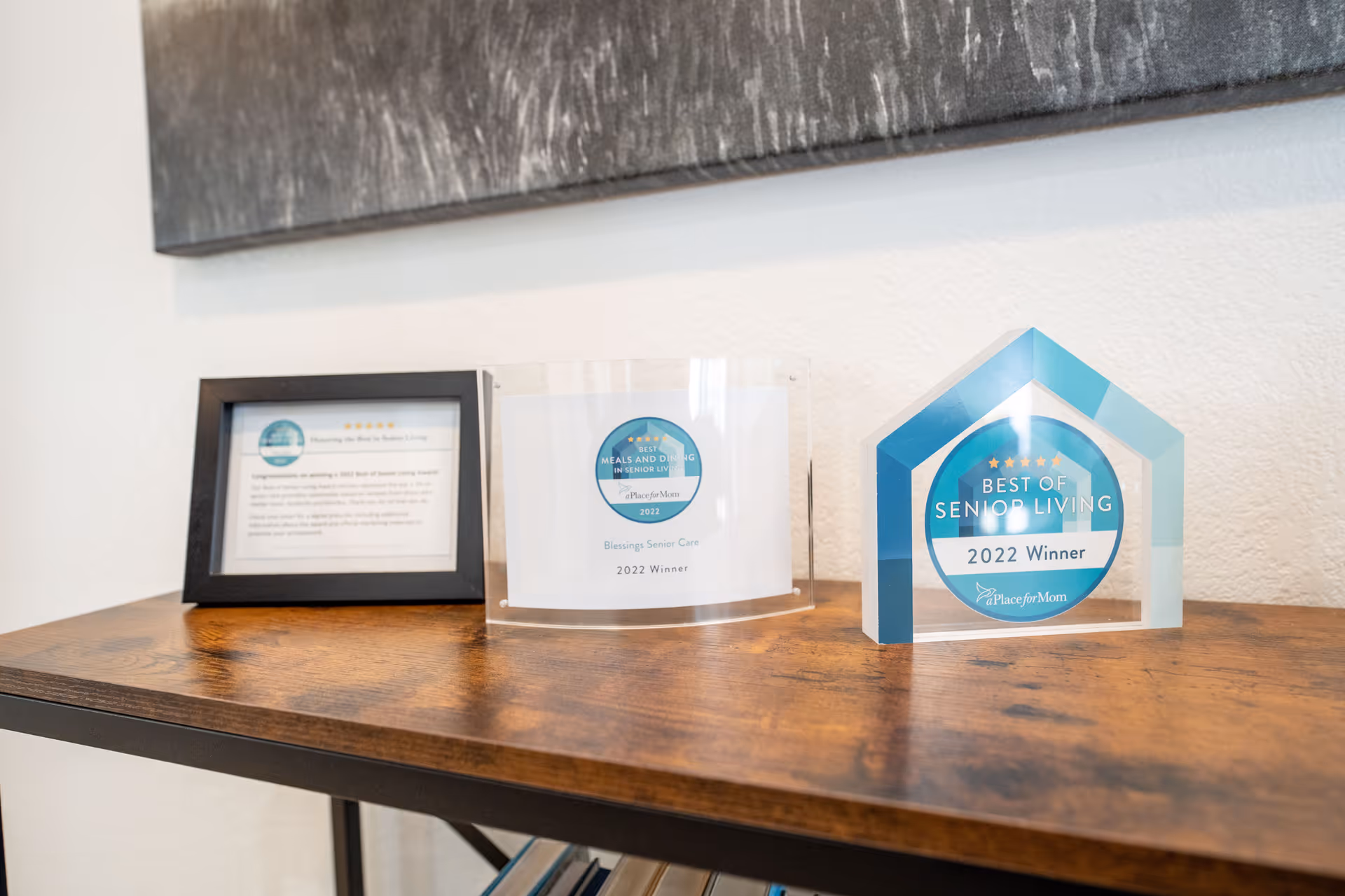 Three awards displayed on a wooden table against a white wall. The awards include a framed certificate and two acrylic plaques recognizing Blessings Senior Care as a 2022 winner for Best of Senior Living and Best Meals and Dining in Senior Living.