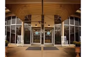 Entrance to a building with large glass double doors, two white rocking chairs on either side, and a covered awning overhead.