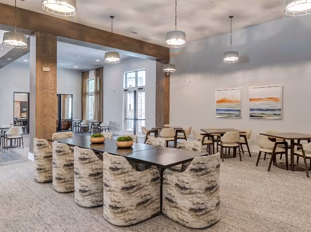 Spacious communal dining/lounge area with modern tables, upholstered chairs, pendant lights, and wall artwork.
