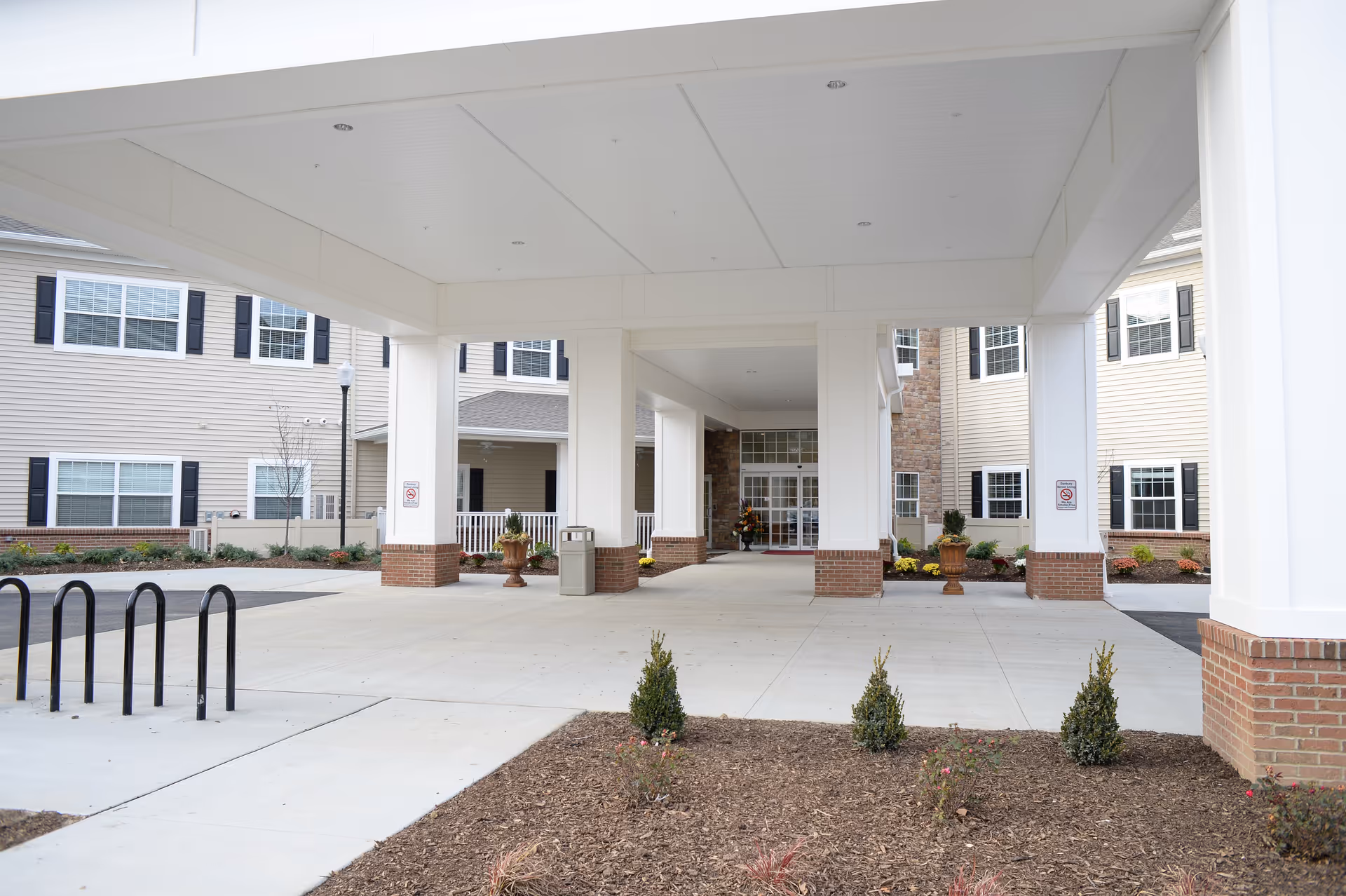 Covered entrance of a senior living facility with columns and a wide driveway.