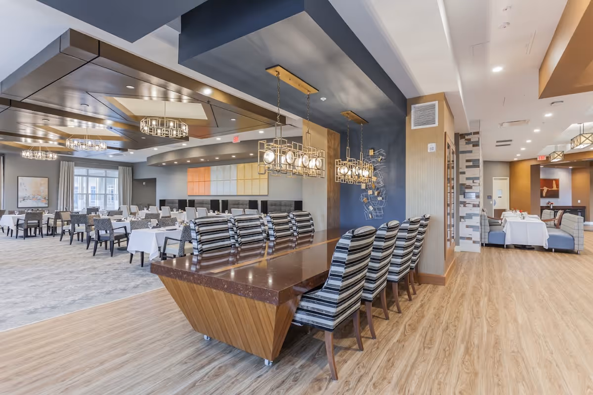 Spacious modern dining room with multiple set tables, a long central table with striped chairs, and decorative pendant lighting.