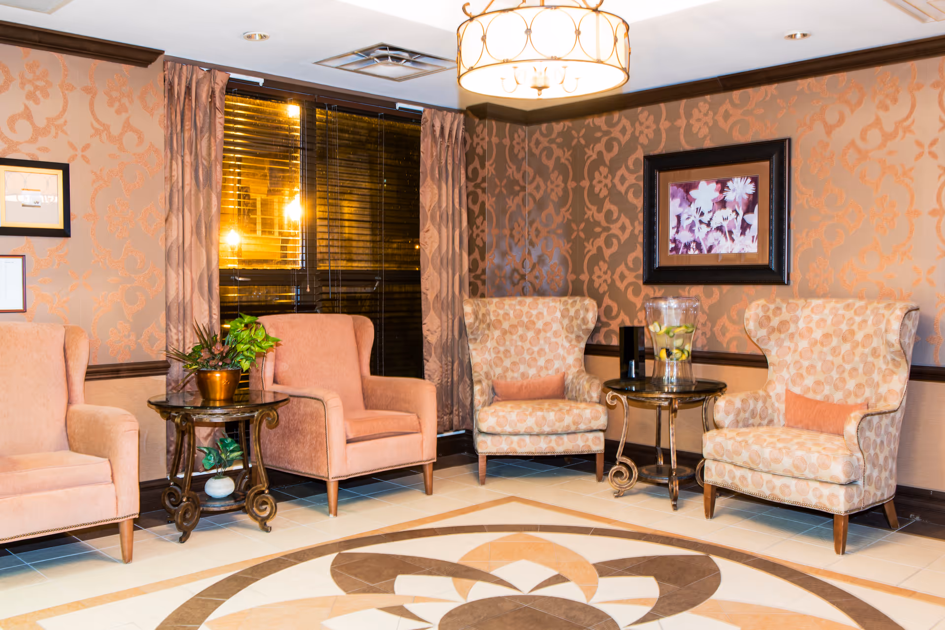 Cozy seating area with upholstered armchairs around side tables, patterned wallpaper, and a decorative ceiling light.