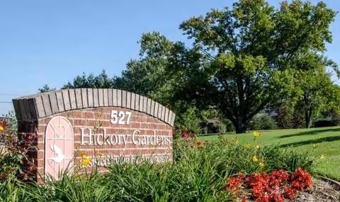 Brick sign reading 527 Hickory Gardens sits on a grassy, flower-filled front yard.